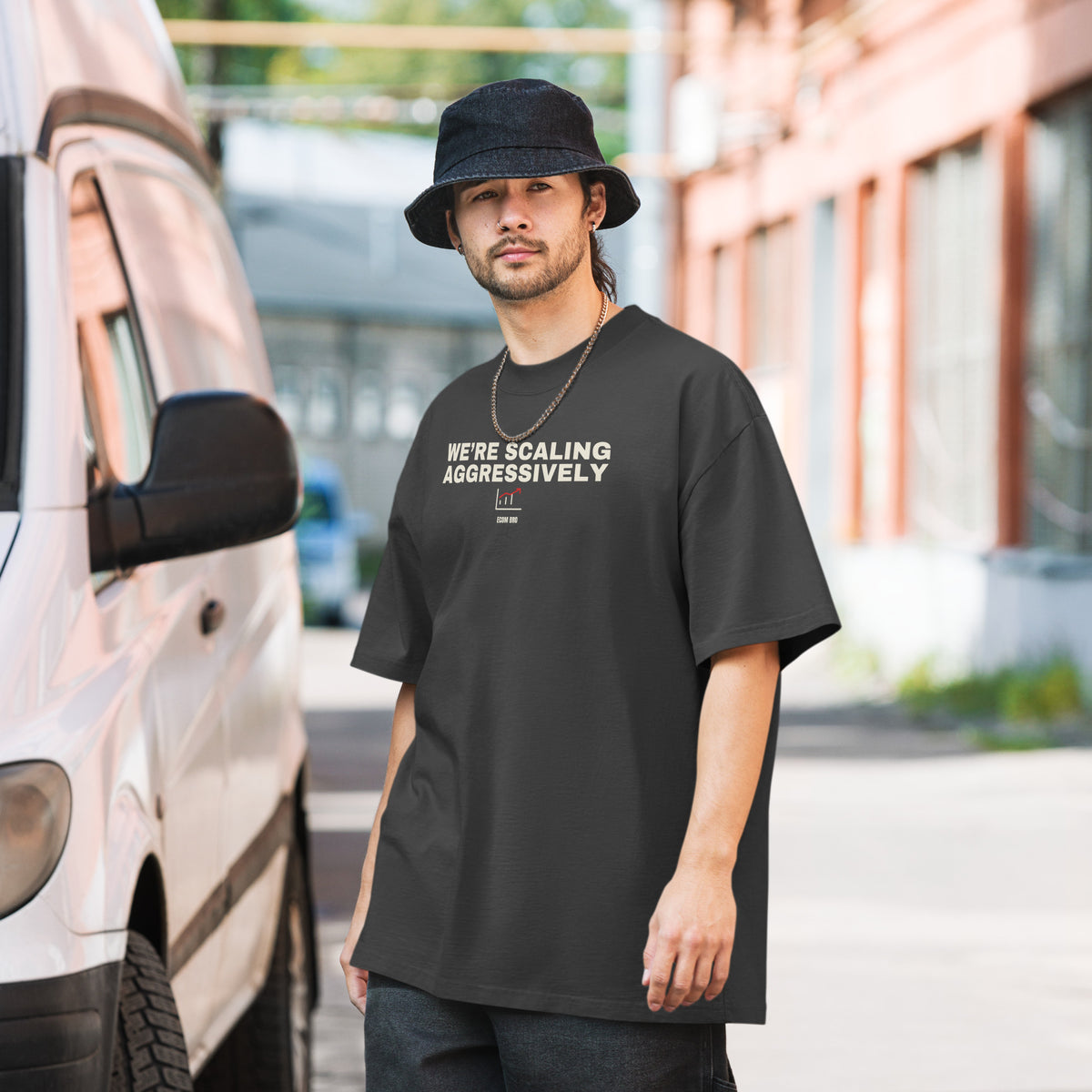 Supplier on-body front mockup: Faded Black oversized tee with large WE’RE SCALING AGGRESSIVELY lettering across the upper chest and a chart below